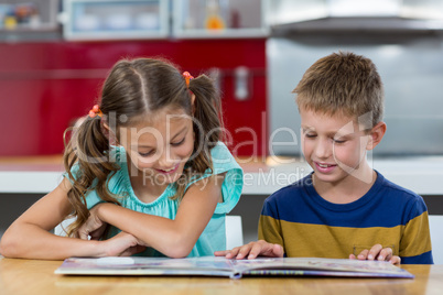 Smiling siblings looking at photo album in kitchen