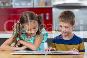 Smiling siblings looking at photo album in kitchen