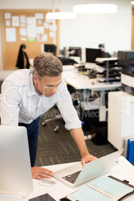 Businessman looking at laptop while leaning on desk