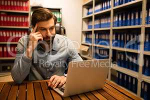 Thoughtful businessman using laptop in file storage room