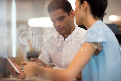 Serious businessman discussing with female colleague on digital tablet