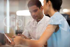 Serious businessman discussing with female colleague on digital tablet