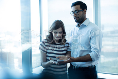Business couple using mobile phone against glass window