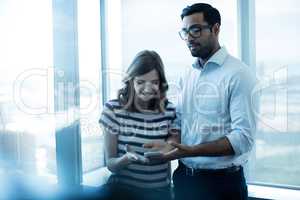 Business couple using mobile phone against glass window