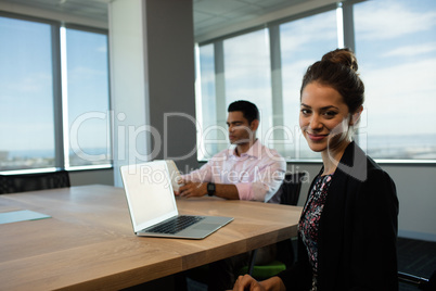 Businesswoman sitting at table with male colleague in background