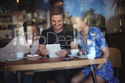 Happy friends using digital tablet while having breakfast