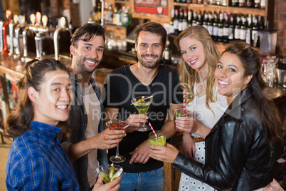 Portrait of smiling friends holding drinks while standing in bar