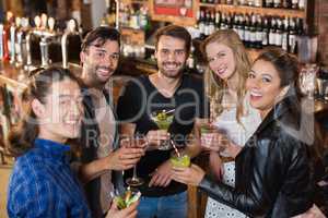 Portrait of smiling friends holding drinks while standing in bar