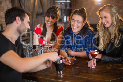 Friends looking at bartender making drinks in pub
