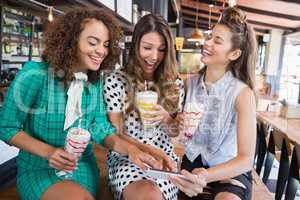 Female friends discussing over mobile phone while sitting in restaurant