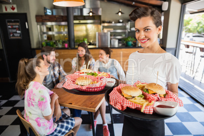 beautiful waitress serving burger to customers sitting in restaurant