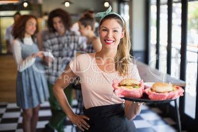 Smiling young waitress serving burger in restaurant