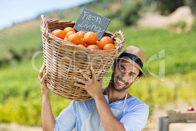 Portrait of smiling farmer carrying by fresh oranges in container
