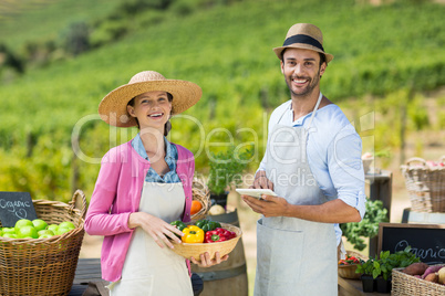 Happy couple holding bell peppers in basket with digital tablet