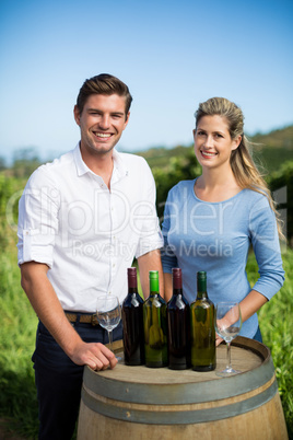 Portrait of friends standing by wine bottles on berrel at vineyard