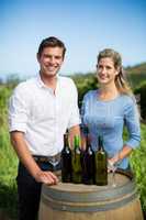Portrait of friends standing by wine bottles on berrel at vineyard