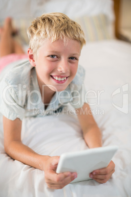 Portrait of smiling boy with digital tablet lying on bed