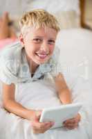 Portrait of smiling boy with digital tablet lying on bed