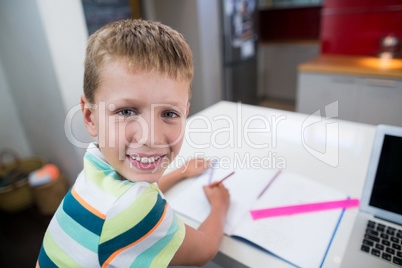 Smiling boy doing his homework in kitchen