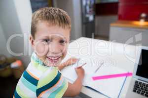 Smiling boy doing his homework in kitchen