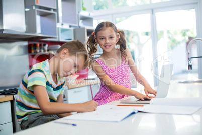 Boy doing his homework while girl using laptop in kitchen