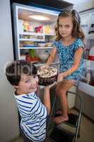 Siblings removing cake from refrigerator in kitchen