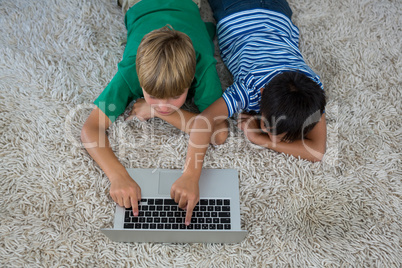 Siblings lying on rug and using laptop in living room