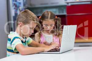 Siblings using laptop and mobile phone in kitchen