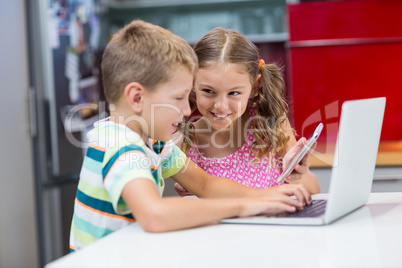 Siblings using laptop and mobile phone in kitchen