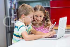 Siblings using laptop and mobile phone in kitchen