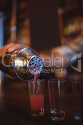 Waiter pouring cocktail drink into shot glasses at counter