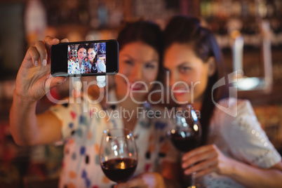 Young women taking a selfie from mobile phone while having a red wine
