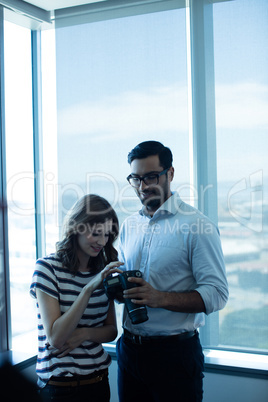 Smiling business couple holding digital camera against glass window