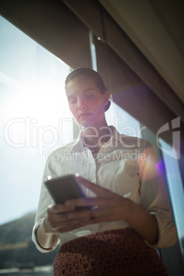 Confident businesswoman using mobile phone in office on sunny day