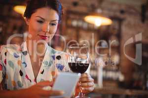 Young woman using mobile phone while having wine