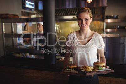 Beautiful woman holding burger and french fries in a tray at restaurant
