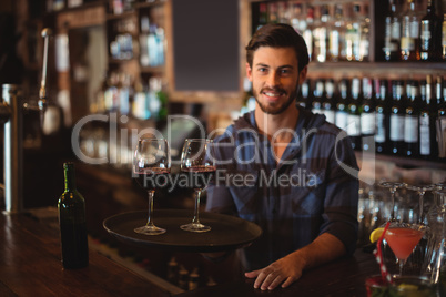 Portrait of bar tender holding a tray with glasses of red wine