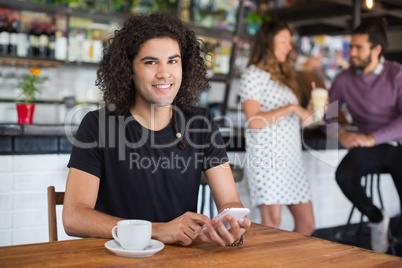 Portrait of young man holding mobile phone while sitting in restaurant