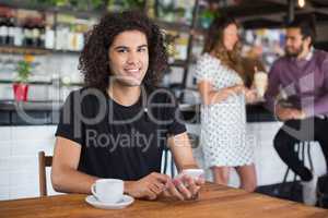 Portrait of young man holding mobile phone while sitting in restaurant