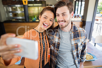 Cheerful friends taking selfie with mobile in restaurant