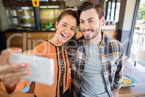 Cheerful friends taking selfie with mobile in restaurant