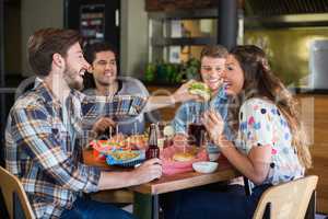 Young man feeding burger to friend in restaurant