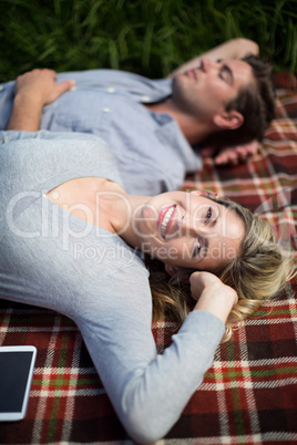 Smiling young woman lying by man sleeping on blanket