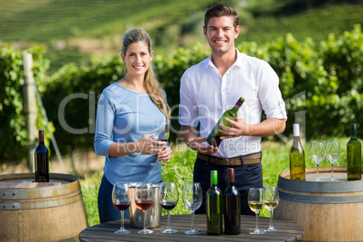 Portrait of friends holding wineglass and bottle by table against vineyard
