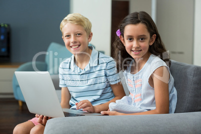 Smiling siblings using laptop in living room