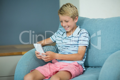 Happy boy sitting on sofa and using mobile phone in living room