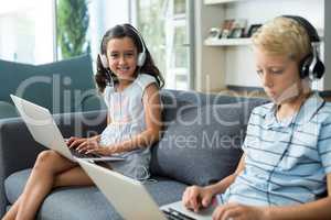 Siblings listening to music while using laptop in living room