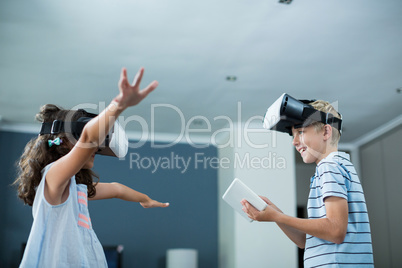 Siblings using virtual reality headset and using digital tablet in living room