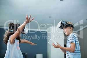 Siblings using virtual reality headset and using digital tablet in living room