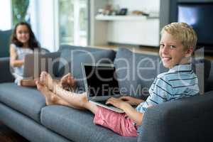 Smiling siblings using laptop in living room